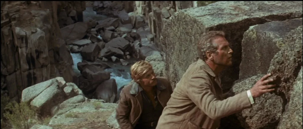Butch Cassidy and the Sundance Kid (1969) movie still: medium — A rugged rocky canyon features large boulders and a stream in the background. Two…