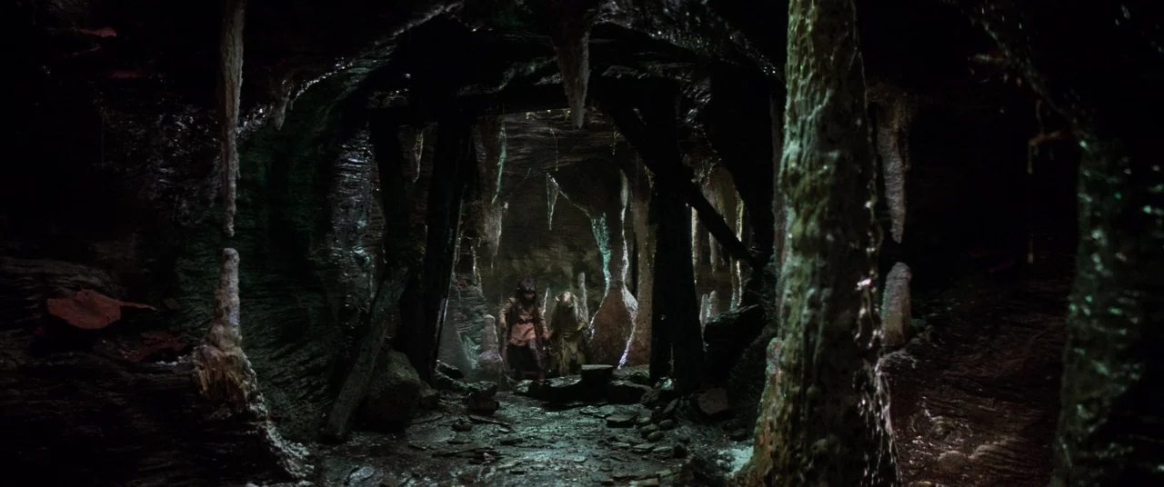 The Dark Crystal (1982) movie still: wide — A subterranean cavern filled with damp rock formations and hanging stalactites. Two small, humanoid…