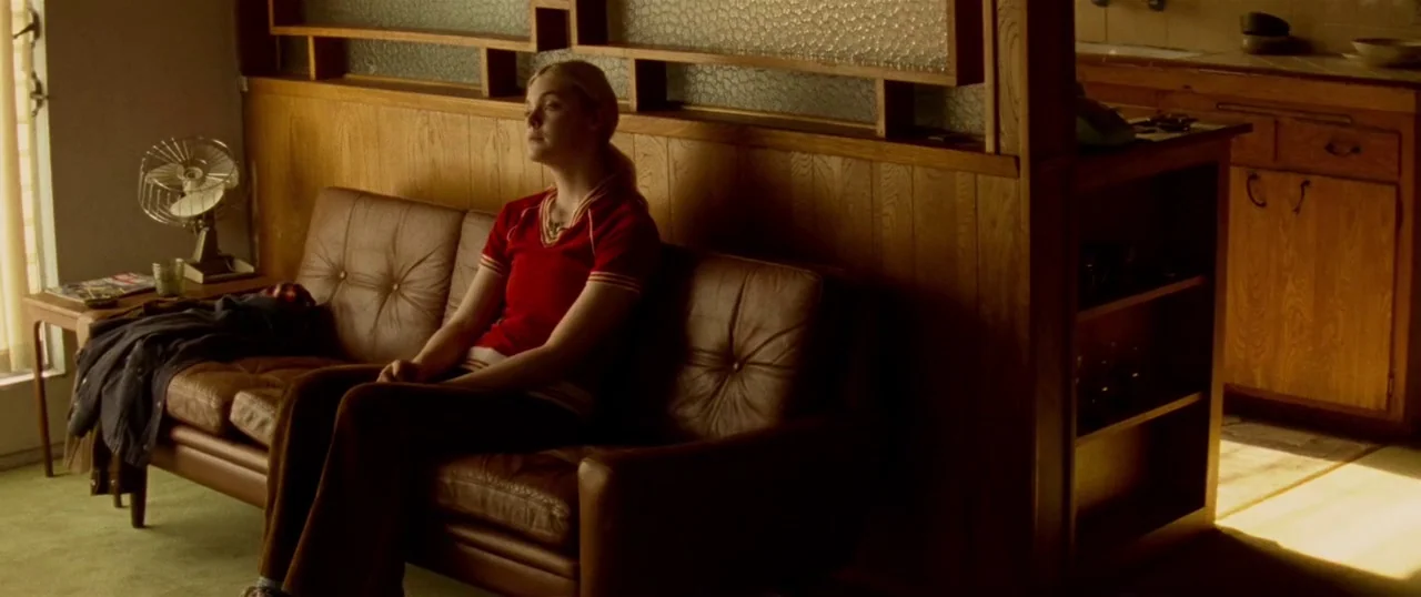 Low Down (2014) movie still: medium — A 1970s living room features wood-paneled walls and a brown leather sofa. A teenage girl sits on the sofa…