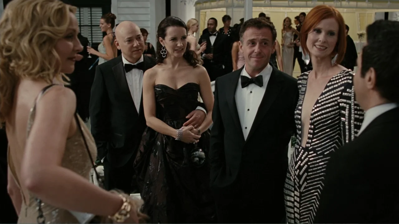 Sex and the City 2 (2010) movie still: fullbody — A group of formally dressed adults gathers at a white tented social event. The individuals stand…