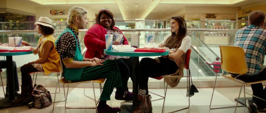 White Bird in a Blizzard (2014) movie still: wide — A food court in a modern indoor shopping mall with multiple dining tables. Four friends sit…