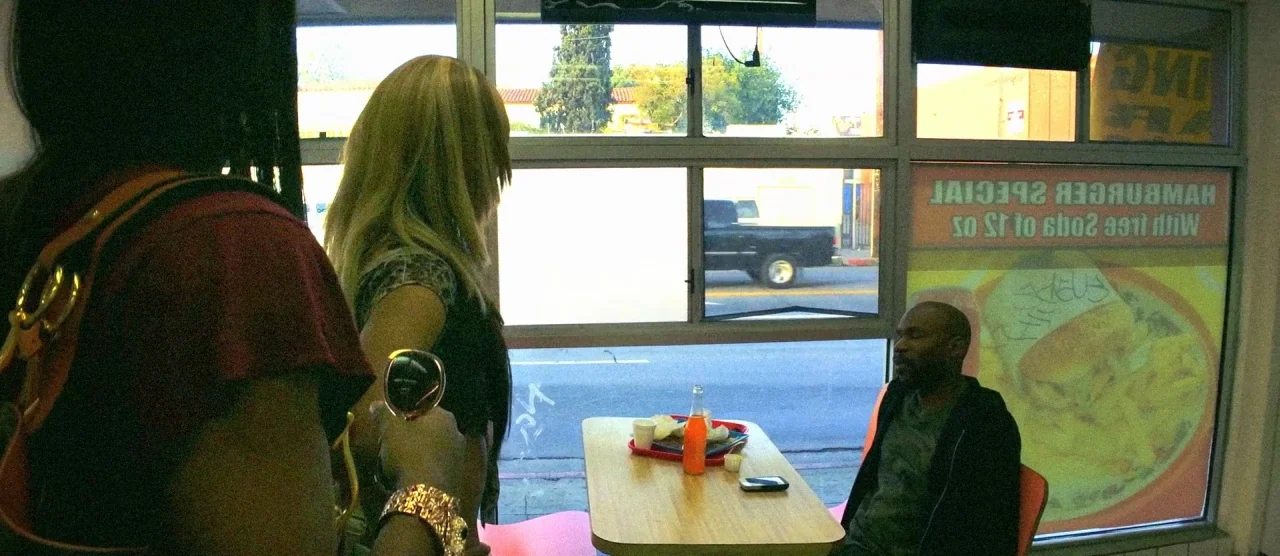 Tangerine (2015) movie still: medium — A fast food establishment with a large window overlooking a street with passing vehicles. A man sits at a…