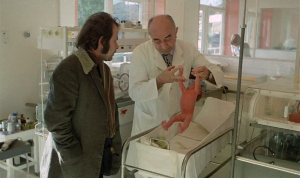 Stroszek (1977) movie still: medium — A clinical hospital room features medical equipment and a sterile white aesthetic. A doctor wearing a white…