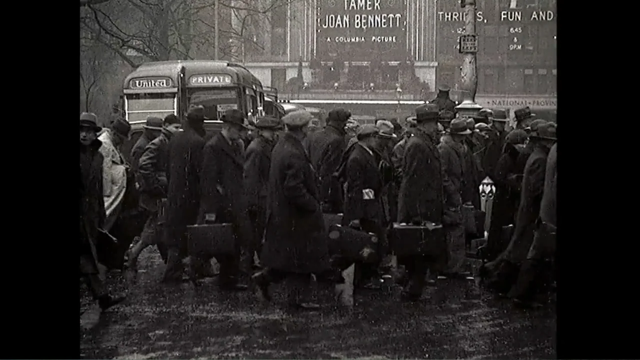 Matthews (2017) movie still: wide — A crowded mid-century city street features a large group of men carrying travel suitcases. Pedestrians walk past…