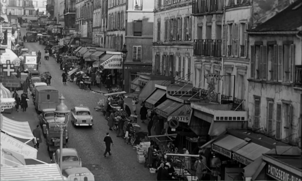 Paris Blues (1961) movie still: establishing — A narrow cobblestone street in 1950s Paris is crowded with outdoor market stalls. Numerous shoppers…