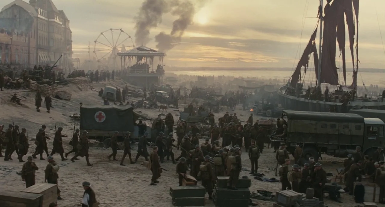 Atonement (2007) movie still: wide — A crowded World War II beach during golden hour features soldiers, trucks, and equipment. A large ship sits on…