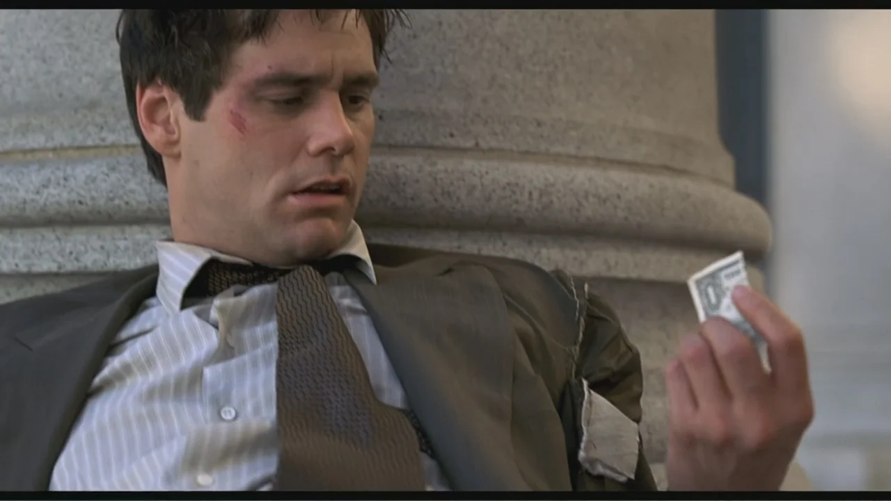 Liar Liar (1997) movie still: medium — A man sits against a large smooth stone column on a set of stairs. He wears a tattered suit and gazes down at…