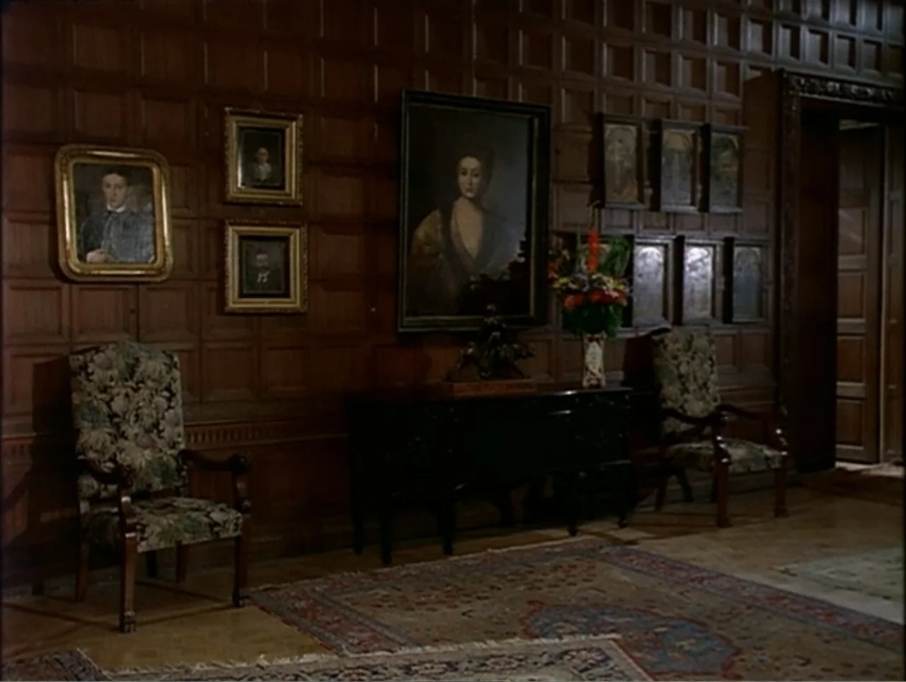A Change of Place (1994) movie still: wide — A wood-paneled manor hallway features ornate portraits and antique floral-patterned chairs. An empty…