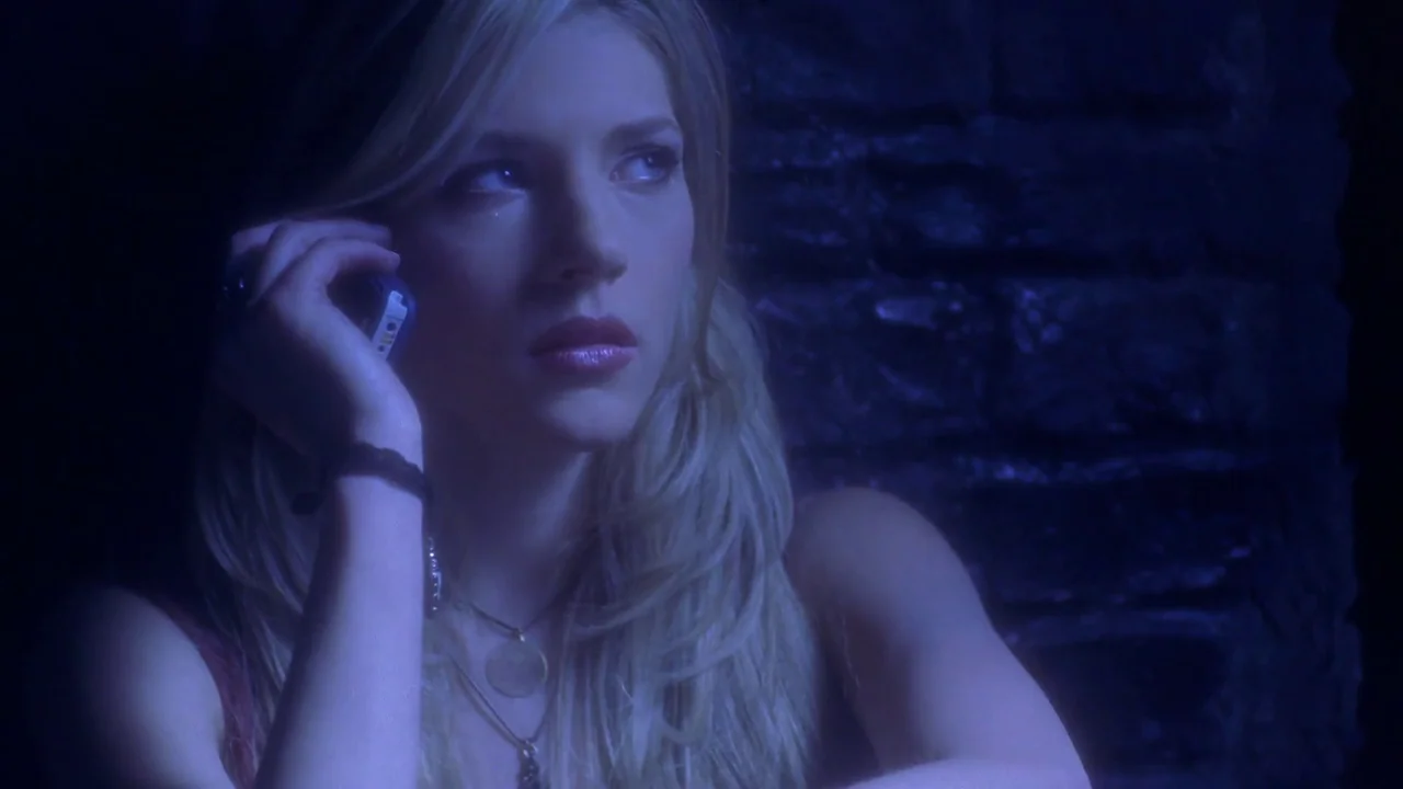 Hellraiser: Hellworld (2005) movie still: closeup — A dark, dimly lit indoor setting features a textured brick-like wall behind the woman. A blonde…