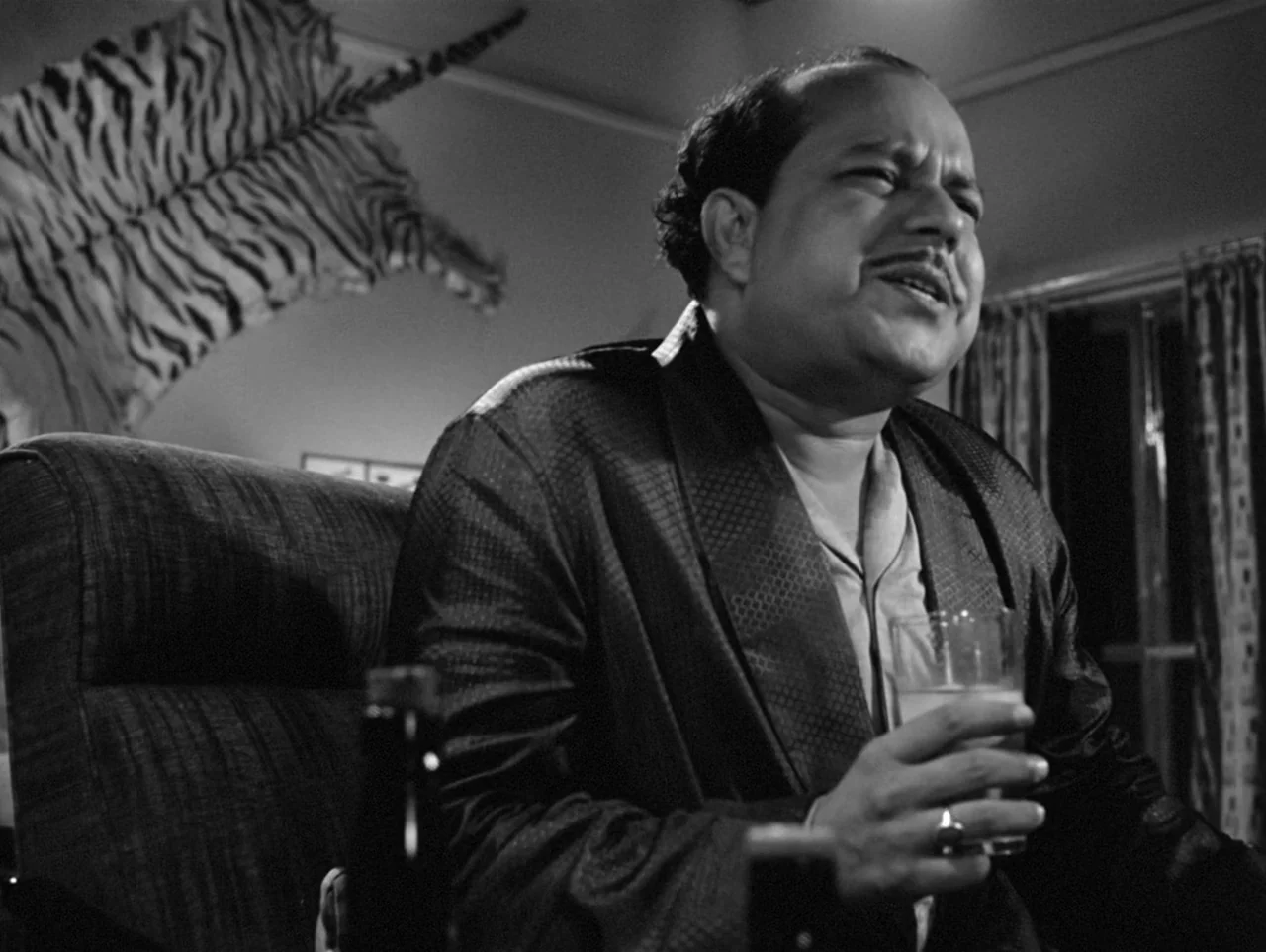 The Coward (1965) movie still: medium — A dark study features a wall decorated with a large tiger skin rug. A middle-aged man sits in a cushioned…