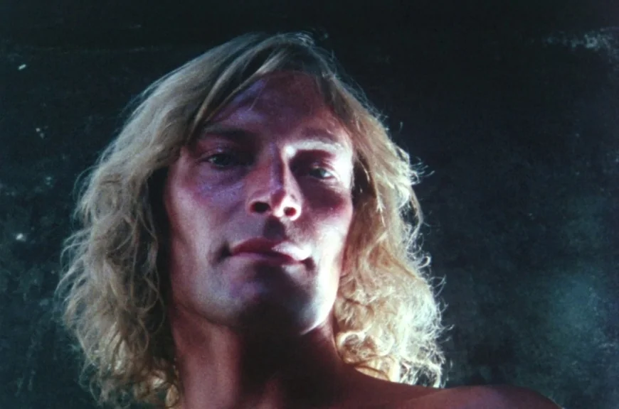 Sebastiane (1976) movie still: closeup — A man stands in an indeterminate dark room with a low-key light source. He gazes directly down into the…