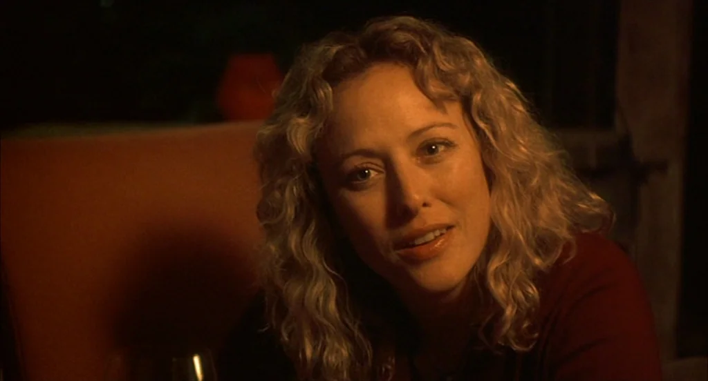 Sideways (2004) movie still: closeup — A dimly lit indoor space featuring a curved booth back. A blonde woman with curly hair looks directly towards…