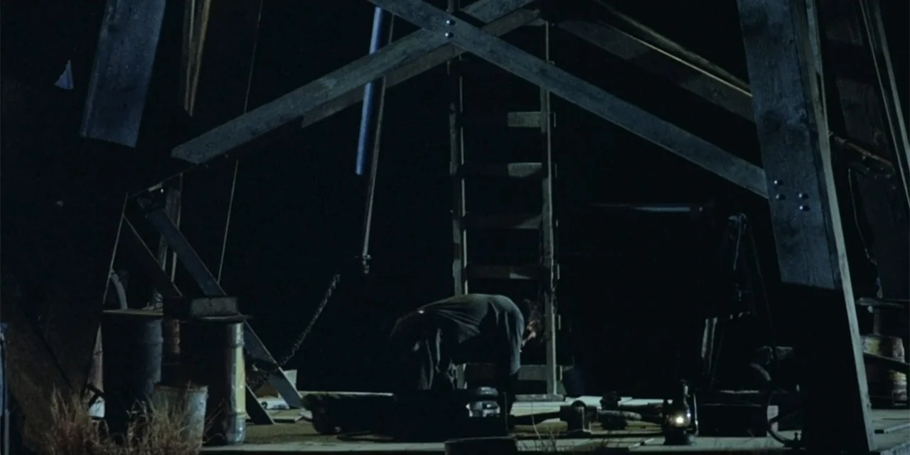 El sótano (2024) movie still: wide — A dark wooden structure contains structural beams and a wooden ladder in the background. A man kneels in the…