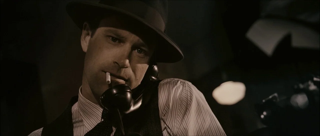The Black Dahlia (2006) movie still: closeup — A darkened interior room features a man holding an old-fashioned telephone receiver. He wears a…