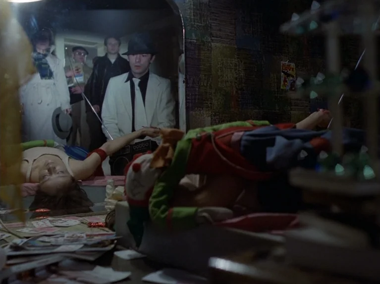 The Third Generation (1979) movie still: medium — A dimly lit room with textured wallpaper and a large mirror reflecting several people. A small…