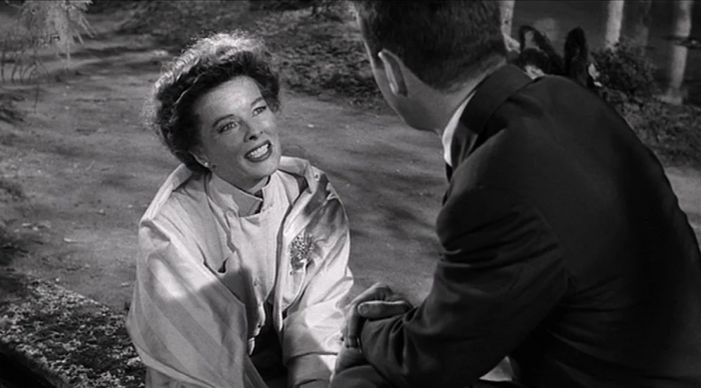 Suddenly, Last Summer (1959) movie still: medium — A woman sits in a park setting with dirt ground and blurred foliage behind. She speaks to a man…
