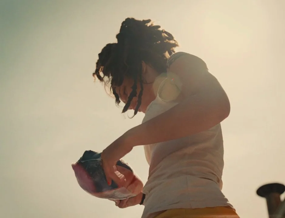 American Honey (2016) movie still: medium — A person stands against a bright, hazy sky on a rooftop area. She looks down at a clear plastic bag…