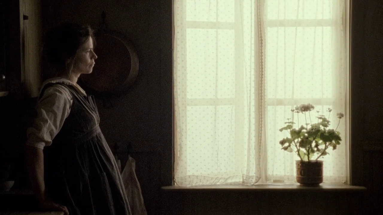 Everlasting Moments (2008) movie still: medium — A dimly lit room features a window with white lace curtains and a potted plant. A woman stands in…