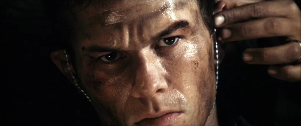 Three Kings (1999) movie still: closeup — A close view of a man's face in a dark, confined space. A hand reaches in to place a mouthguard into his…