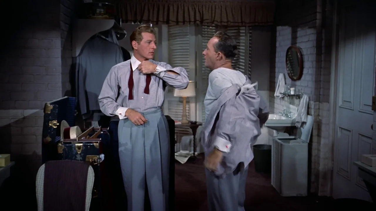 White Christmas (1954) movie still: medium — A furnished 1950s interior space features brick-textured walls and a small vanity area. Two men in…