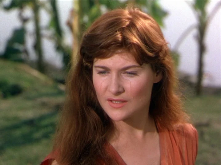 The River (1951) movie still: closeup — A woman stands in a lush tropical setting with blurred palm trees in background. She gazes slightly…