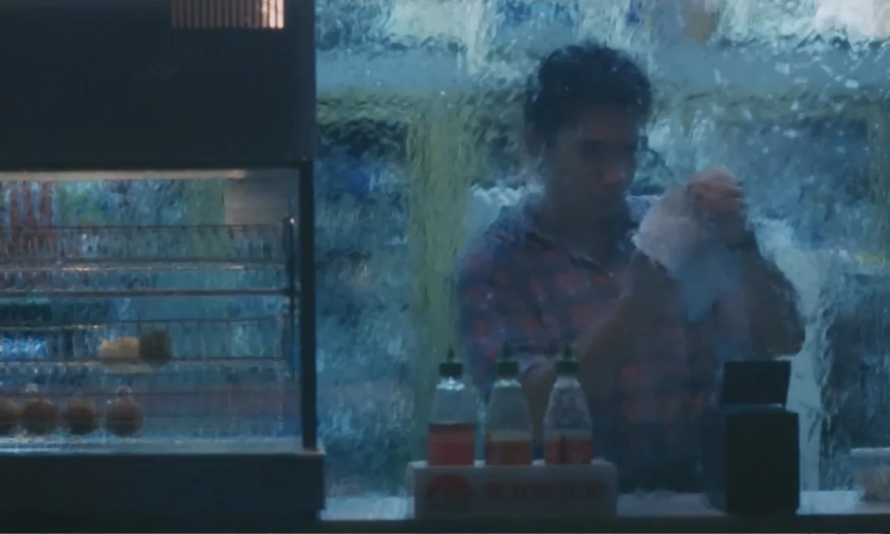 Chungking Express (1994) movie still: medium — A man stands behind a convenience store counter viewed through textured rippled glass. The man is…