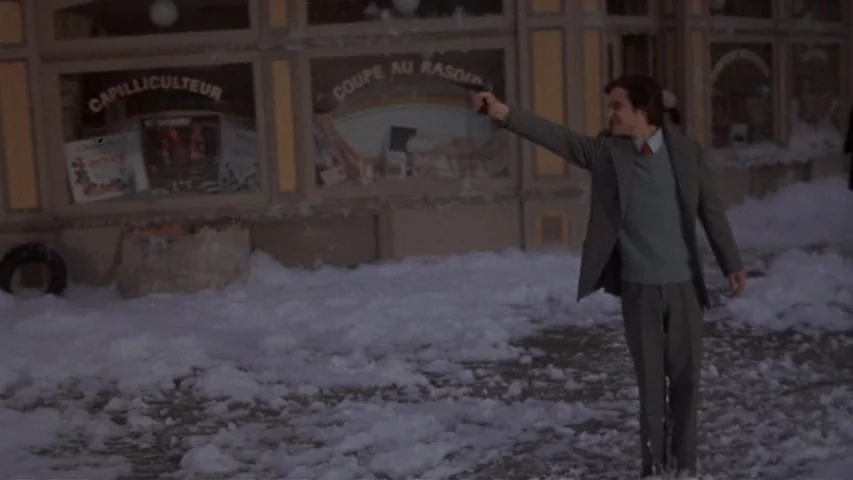 Day for Night (1973) movie still: fullbody — A snowy street in front of a storefront with French text on its window. A man in a business suit stands…