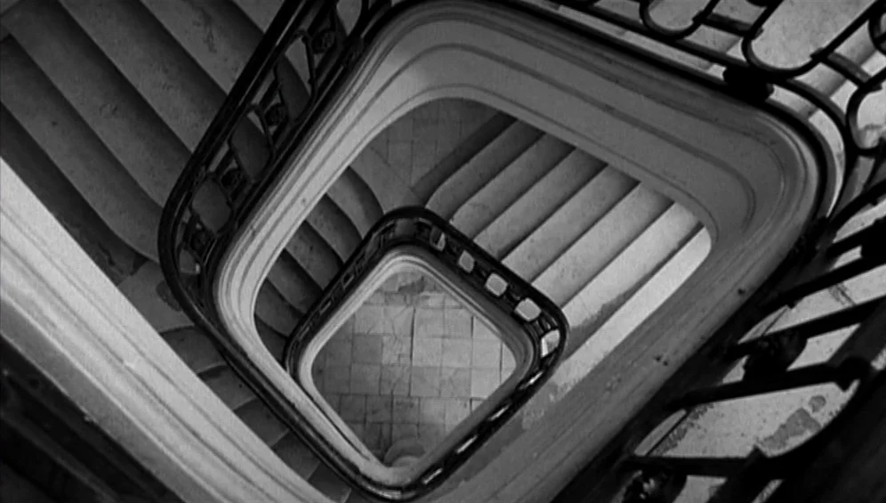The Tango Lesson (1997) movie still: establishing — A spiral staircase with wrought iron railings viewed from directly above. The steps descend…