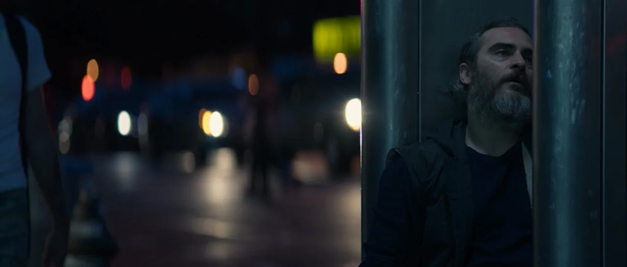 You Were Never Really Here (2017) movie still: medium — An urban sidewalk at night features a man leaning against a large metal pole. Out-of-focus…