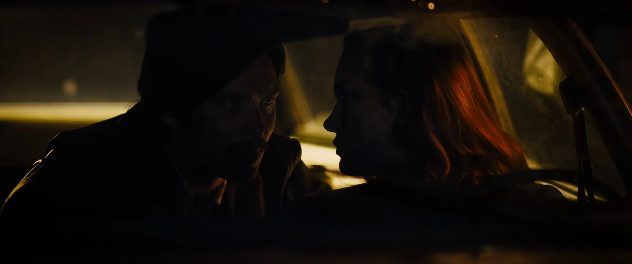 Free Fire (2016) movie still: medium — A dark, cramped car interior lit by external street illumination during the night. A man and a woman sit…