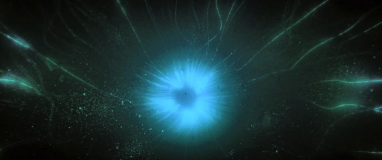 Sea Fever (2019) movie still: closeup — A dark, formless expanse is dominated by a central point of glowing blue light. Thin, bright filaments…