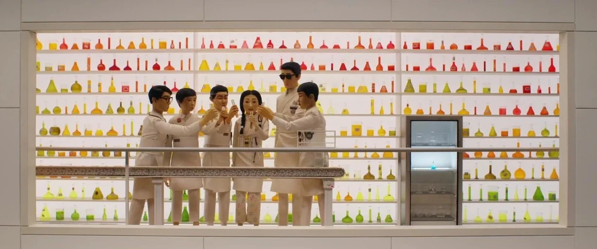 Isle of Dogs (2018) movie still: wide — A symmetrical laboratory interior features white walls and floor-to-ceiling shelves filled with colorful…