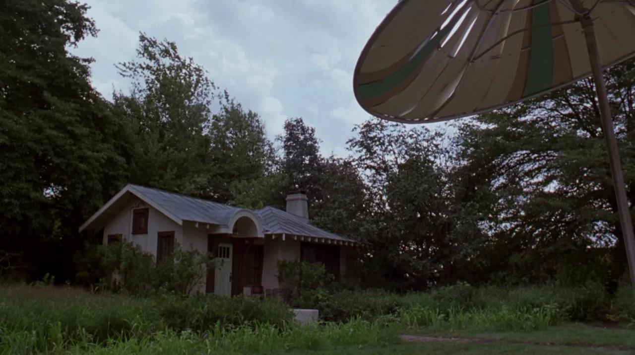 Lady in the Water (2006) movie still: wide — A small cottage sits tucked behind dense green trees in an overgrown lawn area. A large, partially…