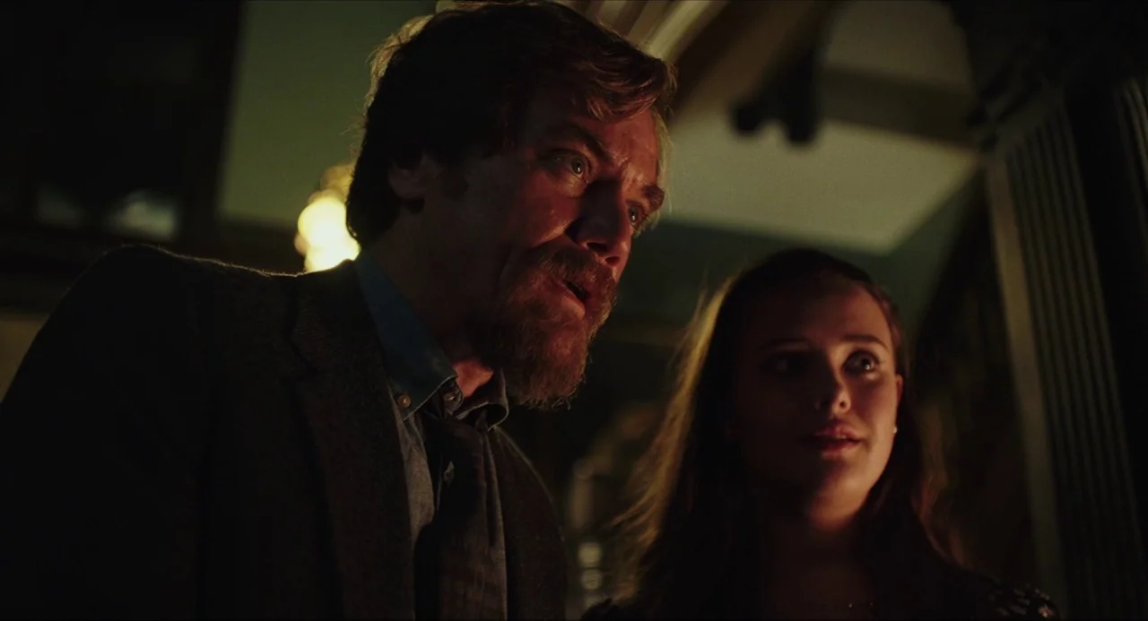 Knives Out (2019) movie still: medium — A dimly lit room at night with dark walls and architectural trim. A man and a woman stand together, looking…
