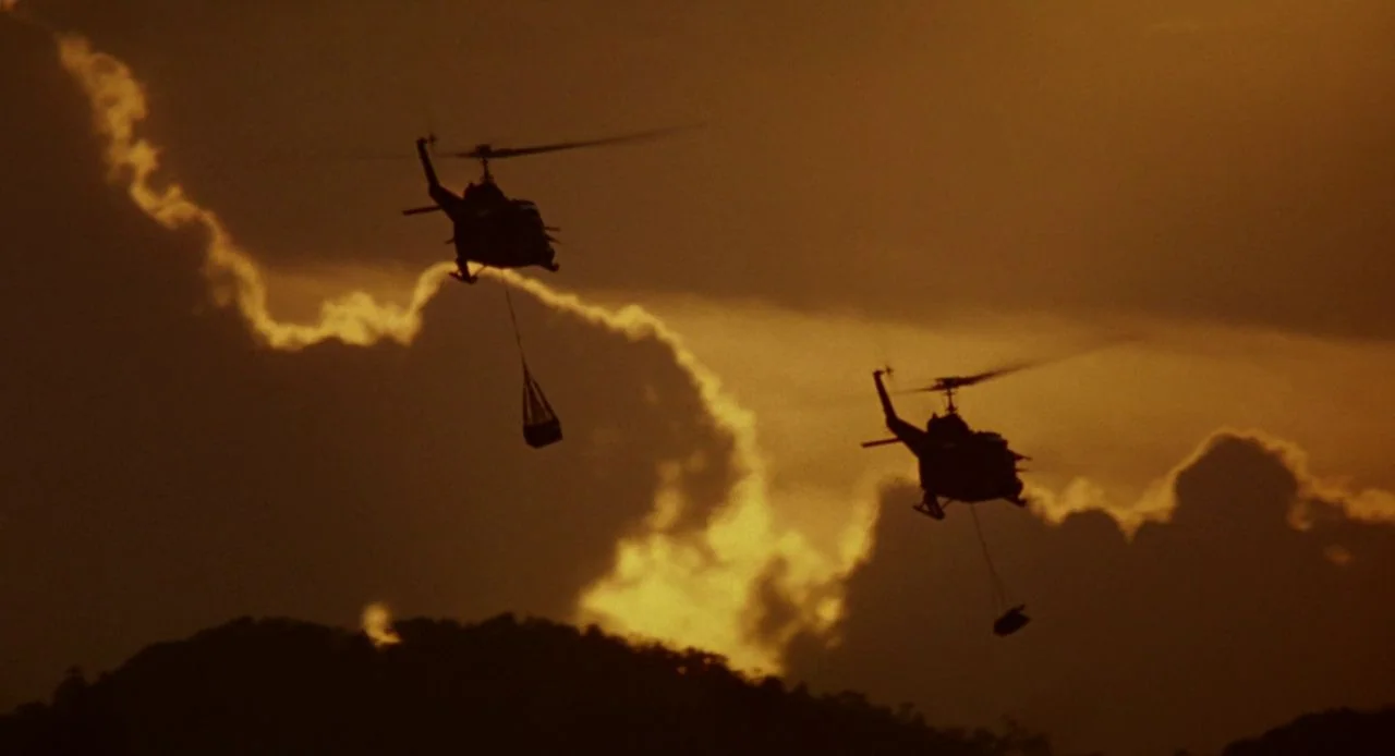 Jacob’s Ladder (1990) movie still: wide — Two transport helicopters are silhouetted against a dense, golden-hued sunset sky filled with clouds. Both…