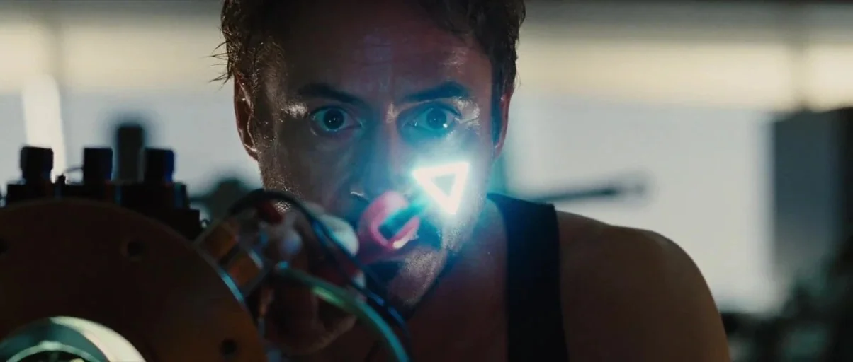 Iron Man 2 (2010) movie still: closeup — A dark laboratory workspace contains advanced mechanical components and complex electrical hardware. A man…