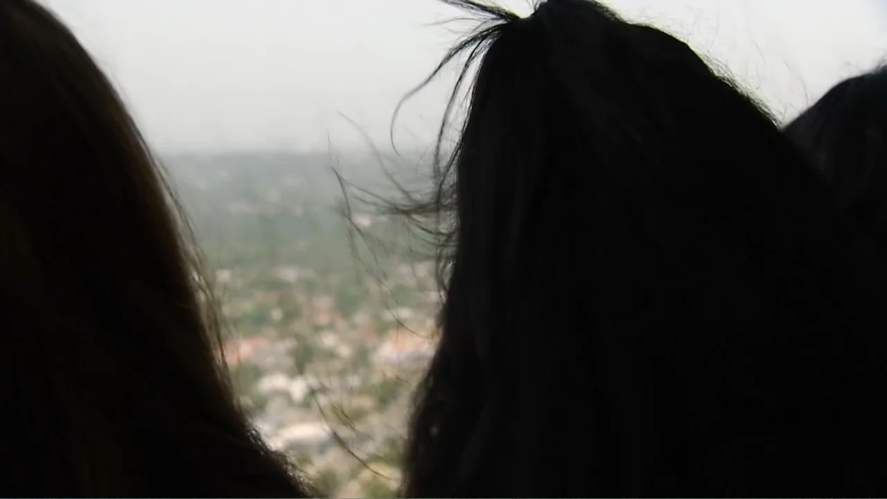 Escape From Saudi (2019) movie still: closeup — A high vantage point overlooks a distant blurred city landscape. Two figures seen from behind watch…