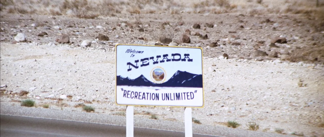 Diamonds Are Forever (1971) movie still: wide — A rectangular sign welcomes visitors to Nevada beside a desolate rocky desert roadside. The white…