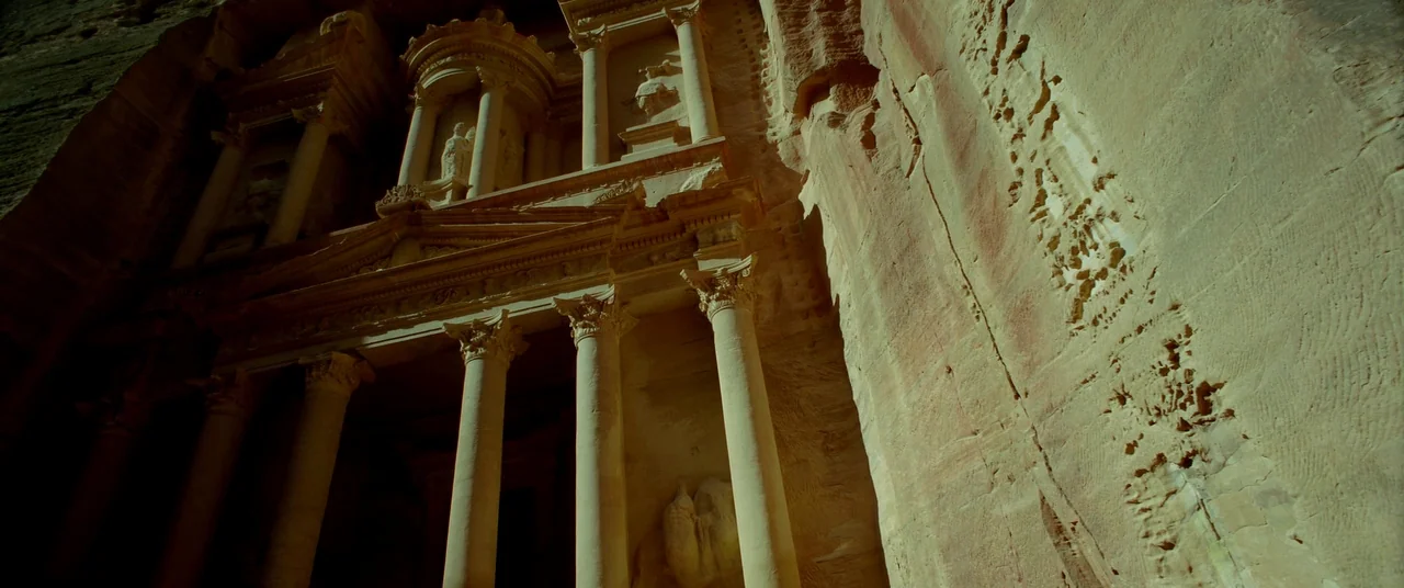 Samsara (2011) movie still: establishing — A massive ancient sandstone facade is carved directly into a high cliff wall. The structure features…