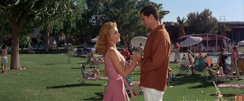 Viva Las Vegas (1964) movie still: fullbody — A sunny resort area features a lawn filled with lounge chairs and palm trees. A man and woman hold…
