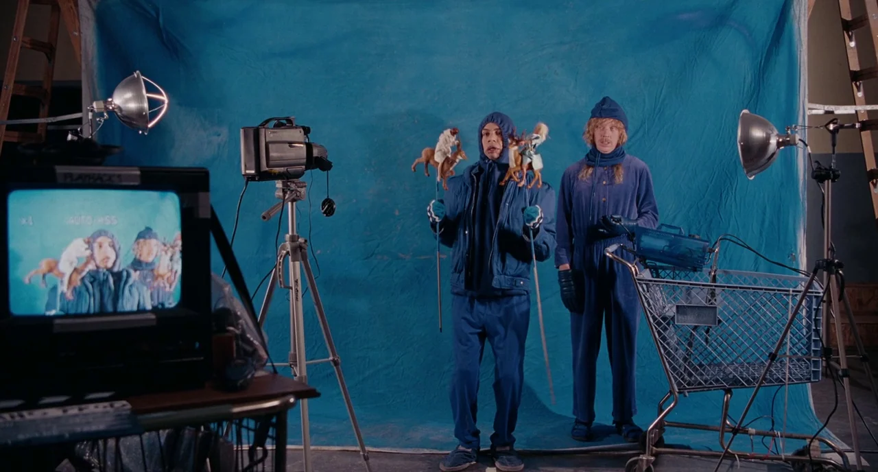 Gentlemen Broncos (2009) movie still: wide — A film studio features a blue backdrop with cameras and lighting equipment scattered around. Two men in…