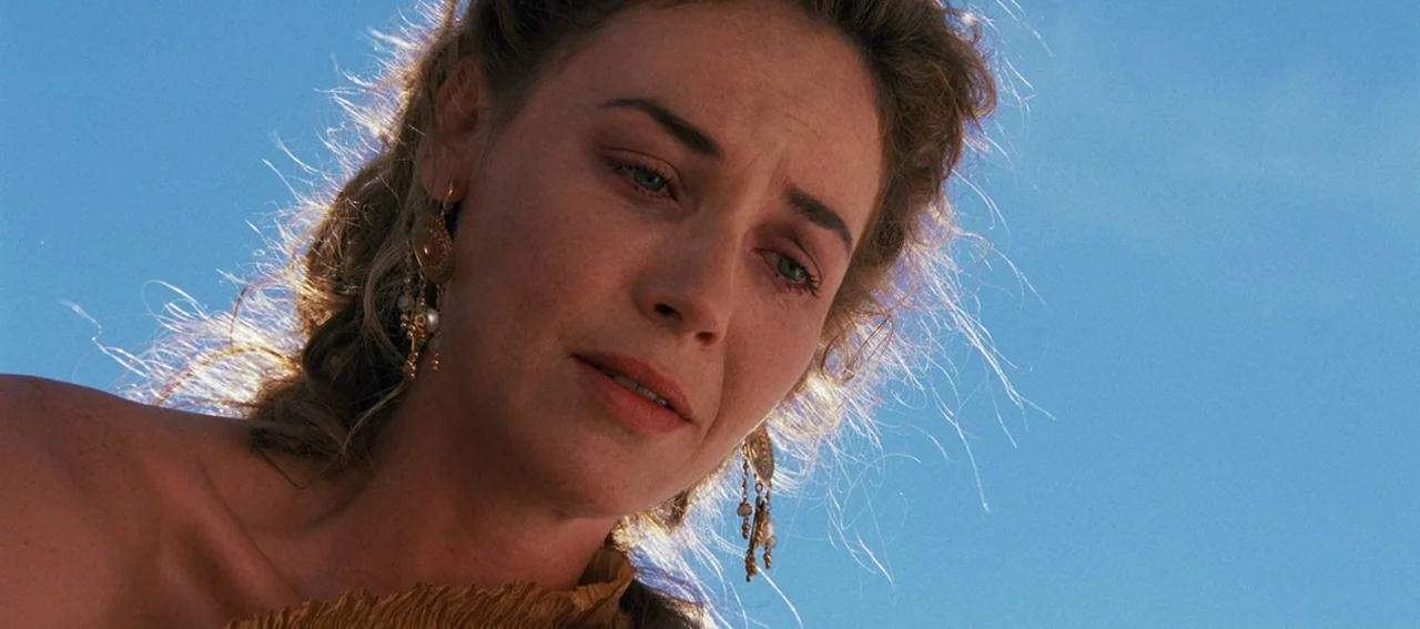 Gladiator (2000) movie still: closeup — A woman stands against a clear, bright blue sky in an outdoor setting. She looks down with tears visible in…
