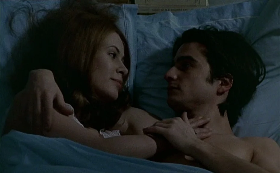 Love on the Run (1979) movie still: medium — A pair of individuals lie in bed under blue covers in a dimly lit room. The two subjects face one…