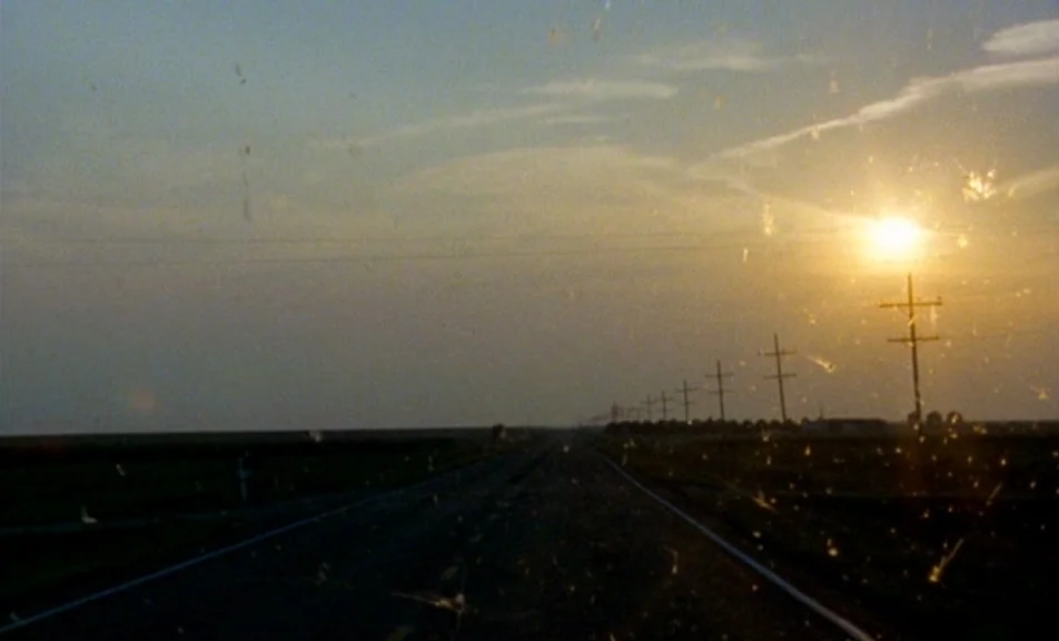 The Brown Bunny (2003) movie still: establishing — A long, flat country road stretches toward the horizon under a setting sun. Several utility poles…