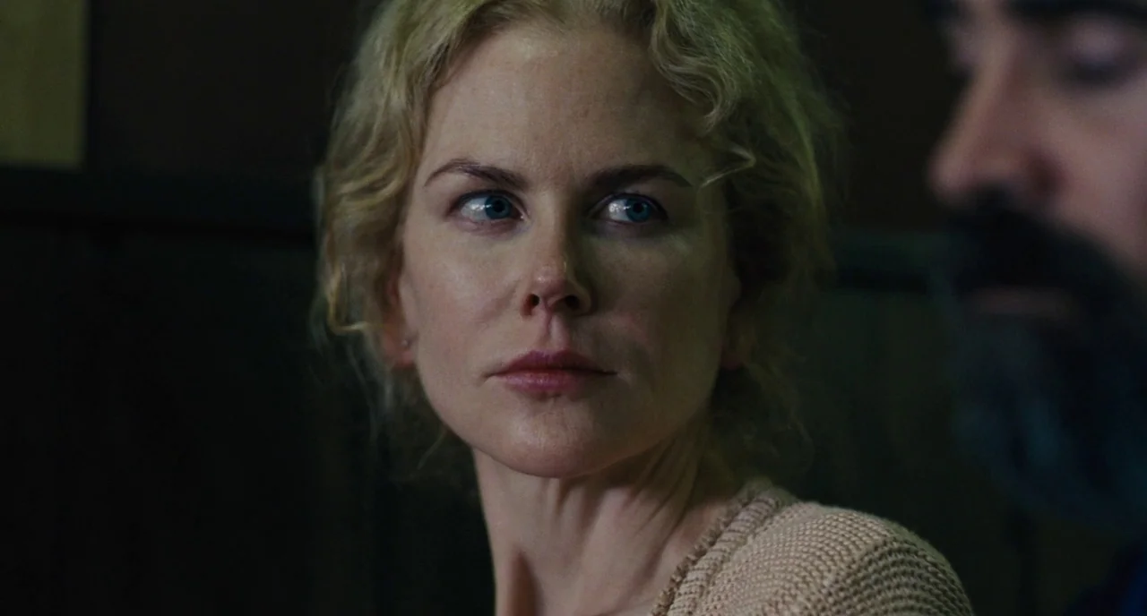 The Killing of a Sacred Deer (2017) movie still: closeup — A dimly lit room with dark walls forms a backdrop for two people. A woman with blonde…