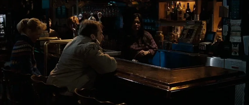 Snow Angels (2007) movie still: medium — A dark wooden bar counter contains a cash register and various drink bottles. A man and a woman sit…