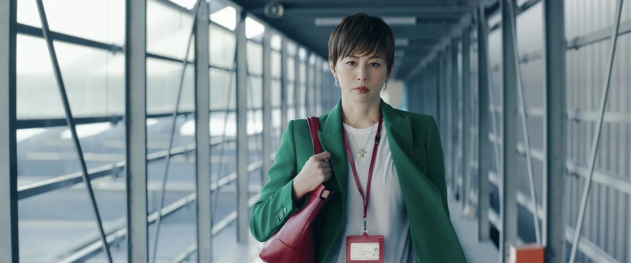 Angel Flight THE MOVIE (2026) movie still: medium — A woman walks down a long, modern, industrial-style pedestrian bridge made of glass and steel.…