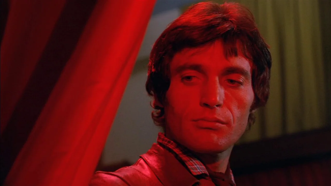 Death Occurred Last Night (1970) movie still: closeup — A man stands in an interior space lit by a bright, directional red light. The man looks…