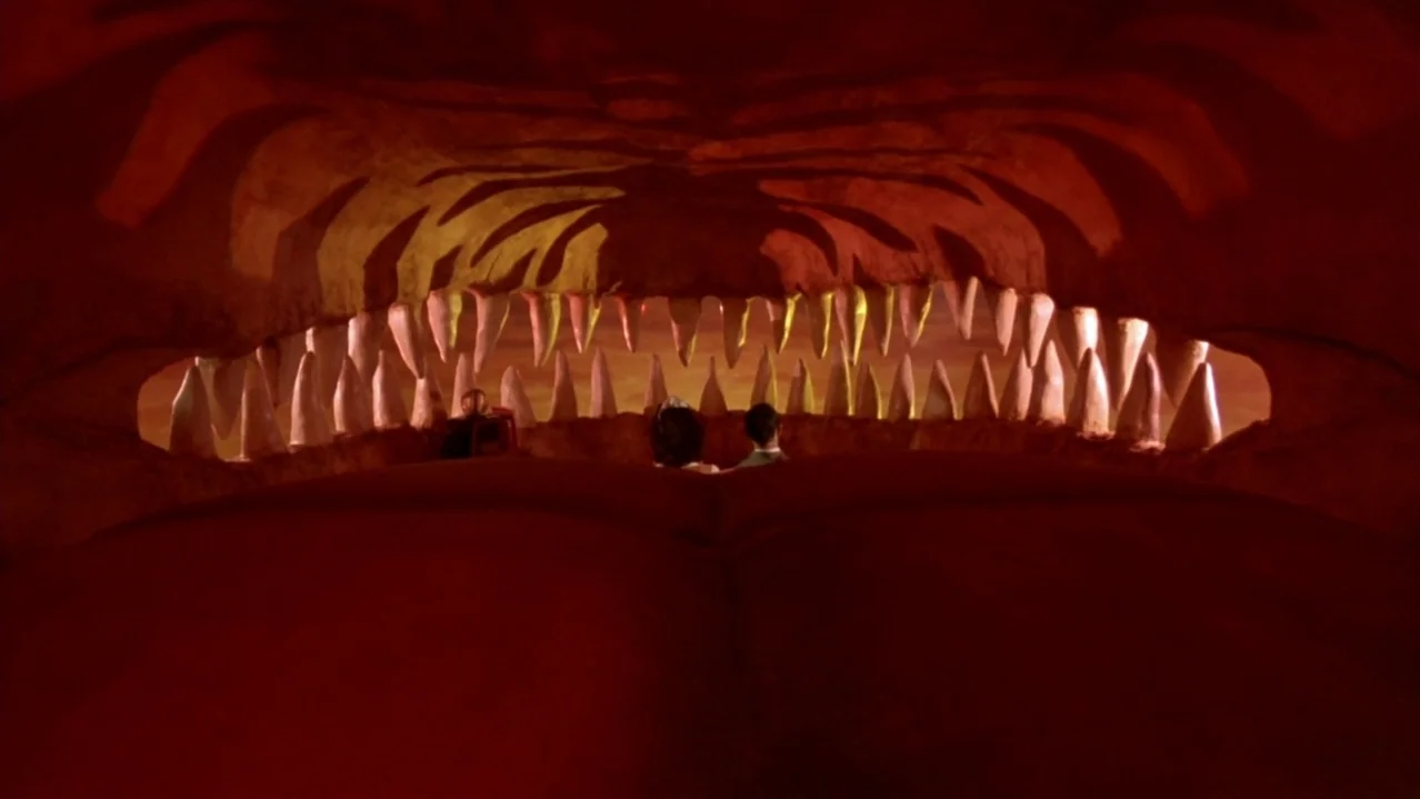 Pee-Wee’s Big Adventure (1985) movie still: wide — A drive-in theater shows a movie featuring an enormous monster mouth on screen. Two people sit in…