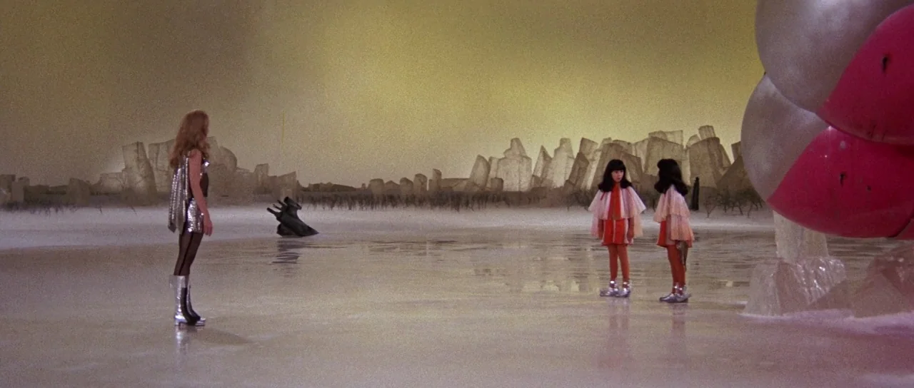 Barbarella (1968) movie still: wide — A flat white frozen landscape stretches toward a backdrop of jagged, ice-like structures. A woman in silver…